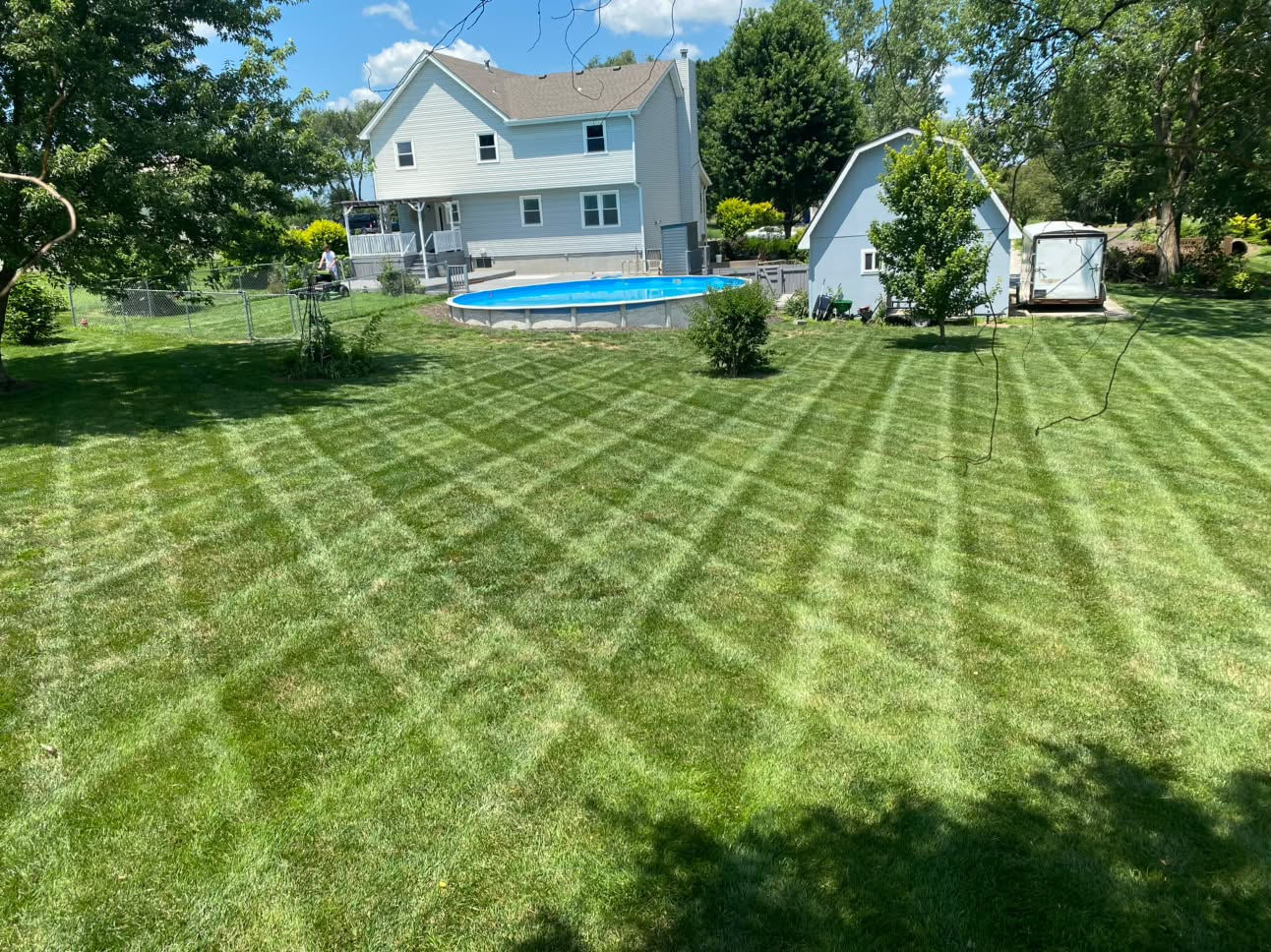 Freshly mowed backyard with lawn stripes beside a home and above-ground pool